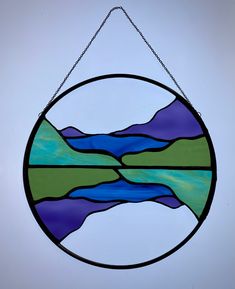 a circular stained glass window hanging from a chain with mountains and water in the background