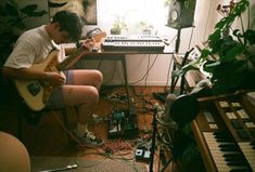 a man sitting in front of a keyboard playing an electric guitar while wearing shorts and socks