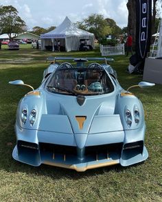 a blue sports car parked on top of a lush green field next to a white tent