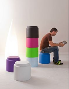 a man sitting on top of a stool next to stacks of different colored plastic cups