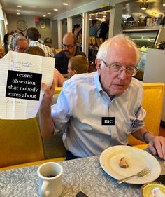 an older man sitting at a table holding up two pieces of paper with words written on them