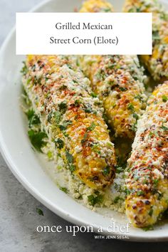 a white plate topped with corn on the cob covered in parmesan cheese