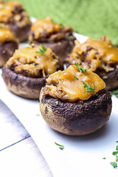 several stuffed mushrooms with cheese on them sitting on a white plate next to green napkin