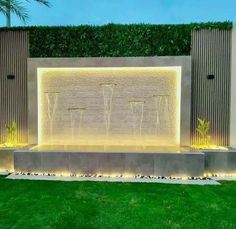 an outdoor water fountain with lights on the sides and grass in front of it at night