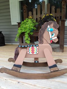 a wooden rocking horse sitting on top of a wooden deck next to a planter