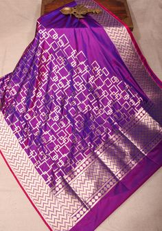 The Banarasi Katan Silk Saree in a stunning purple dual tone is a striking blend of elegance and artistry. Featuring an exquisite geometric jaal pattern, it showcases intricate patterns that reflect the rich heritage of Banarasi craftsmanship. The dual tone adds depth and sophistication, allowing the saree to radiate a captivating allure. Crafted from luxurious Katan silk, it drapes beautifully, making it ideal for special occasions and celebrations. This saree is a perfect choice for those seeking to make a bold yet refined statement with a touch of traditional charm SILK MARK CERTIFIED This saree is ready to wear with fall and pico done. Handmade silk tassels adorn the pallu and add more grace to it. An unstitched blouse fabric is included. *Note: There may be minor variations in the sha Luxury Purple Blouse With Zari Weaving, Luxury Katan Silk Unstitched Saree Suit, Luxury Purple Katan Silk Pre-draped Saree, Luxury Purple Katan Silk Traditional Wear, Luxury Katan Silk Unstitched Blouse, Luxury Unstitched Katan Silk Blouse, Luxury Silk Saree For Celebration, Luxury Unstitched Silk Mark Certified Saree, Luxury Katan Silk Saree Fabric