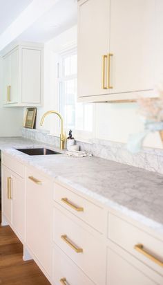 a white kitchen with marble counter tops and gold pulls on the cabinet doors is pictured in this image