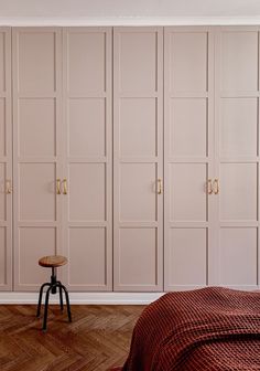 a bedroom with pink walls and wooden floors is pictured in this image, there are two stools on one side of the bed