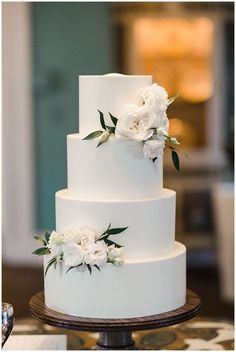 a three tiered white wedding cake with flowers on the top and bottom, sitting on a table