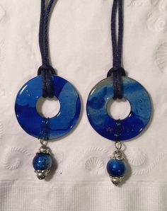 two necklaces with blue beads hanging from them on a white cloth covered tablecloth