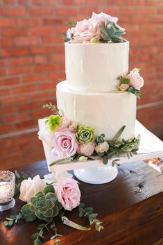 a white wedding cake with pink flowers and succulents sits on a table