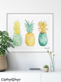 three pineapples in different colors are displayed on a white shelf next to a potted plant