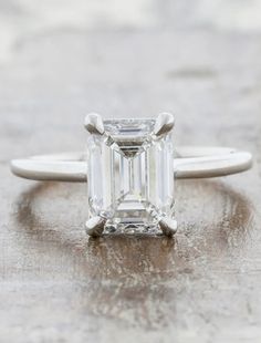 an emerald - cut diamond ring sits on a wooden surface in this close up photo