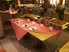 people are sitting at tables with food on them in a large dining room filled with red and white checkered tablecloths