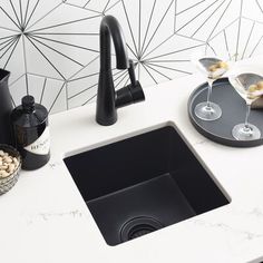 a kitchen sink sitting under a faucet next to a counter top with wine glasses on it