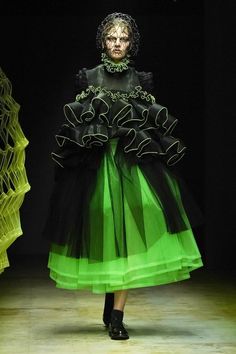 a woman is walking down the runway wearing a green dress with black ruffles