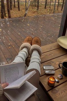 a person sitting at a table reading a book and holding a cup with tea in it