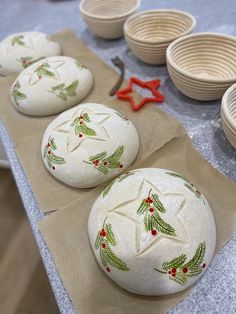 three white balls decorated with holly leaves and red berries are sitting on wax paper next to bowls