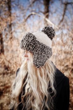 a man with long blonde hair wearing a knitted hat in front of some trees