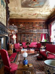 a living room filled with red couches and chairs next to a fire place in front of a painting on the wall