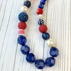 Here's a real firecracker of a necklace that's ready to celebrate 4th of July with you! Our Lenora Dame signature Queen Mum style large beaded necklace in patriotic red, white and blue beads. A harmonious mix of beads from cat's eye, pearl, rhinestone pave, big red and blue bumpy pave, navy with glitter and oversized navy faceted Lucite. The perfect necklace to accessorize for a July 4th BBQ, Memorial Day, Military ceremonies, and other military occasions. The necklace measures 18.5-Inches with Red Patriotic Necklace For 4th Of July, Patriotic Round Beads Necklace As Gift, Patriotic Round Beads Necklace Gift, Festive Blue Necklaces With Large Beads, Festive Blue Necklace With Large Beads, Patriotic Blue Jewelry With Colorful Beads, Patriotic Blue Beaded Necklace For Gifts, Patriotic Blue Necklace For Gift, Patriotic Blue Beaded Necklace For Gift