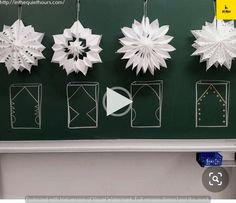 paper snowflakes are hanging on the wall in front of a blackboard with white writing