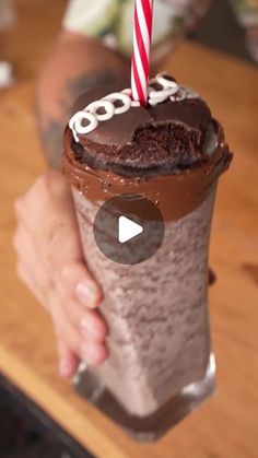 a person holding up a chocolate milkshake with a candle in it's cup