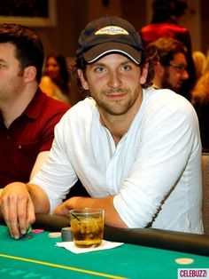 a man sitting at a table with a drink in front of him and people watching