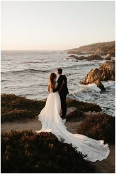 a bride and groom standing on the cliff overlooking the ocean