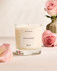 a candle sitting next to pink roses on a white table with the words english rose in front of it