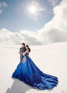 a man and woman are standing in the snow with their arms around each other wearing blue dresses