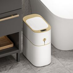 a white and gold trash can next to a bath tub in a bathroom with grey walls