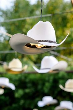 several hats hanging from wires in front of some trees and bushes, with one white hat on the string