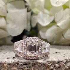 an emerald cut diamond ring on top of a rock with flowers in the back ground