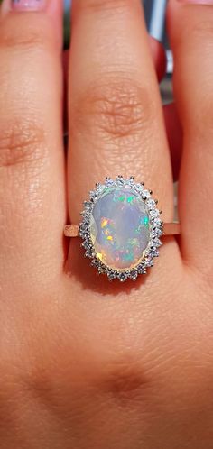 a woman's hand holding an opal and diamond ring