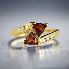 two yellow gold rings with garnetia and white diamonds on the sides, sitting on a silver surface