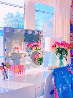 a white desk topped with lots of pink flowers next to a mirror and vase filled with flowers