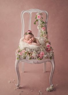 a baby is laying on top of a white chair with pink flowers and greenery