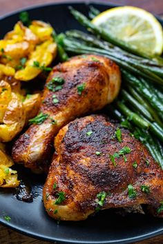 chicken, potatoes and asparagus on a black plate with lemon wedged green beans