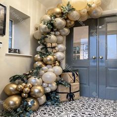 the balloon arch is decorated with gold and silver balloons, greenery, and presents