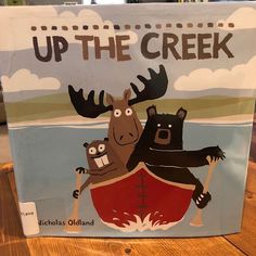 an up the creek sign with moose and bear on it's back in front of a wooden table