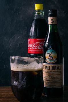 two bottles of soda and a glass with ice on a wooden table next to each other