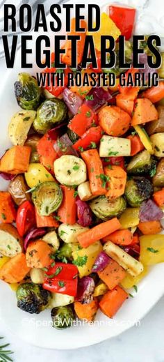 roasted veggies with smashed garlic on a white plate next to lemons and herbs