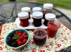 raspberry jam and fresh berries sit on a table with two cups of jelly