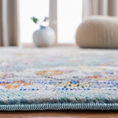 a close up of a rug on the floor with a vase in the back ground