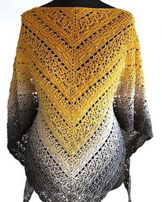 a woman wearing a yellow and black crocheted shawl on top of a mannequin