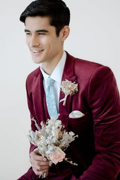 a man in a red suit holding a bouquet of flowers and smiling at the camera