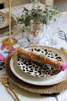 a table set with place settings and gold utensils, including an orange napkin