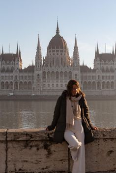 a woman is sitting on a ledge near the water