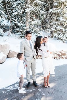 a man and woman standing next to a little boy in the snow with trees behind them